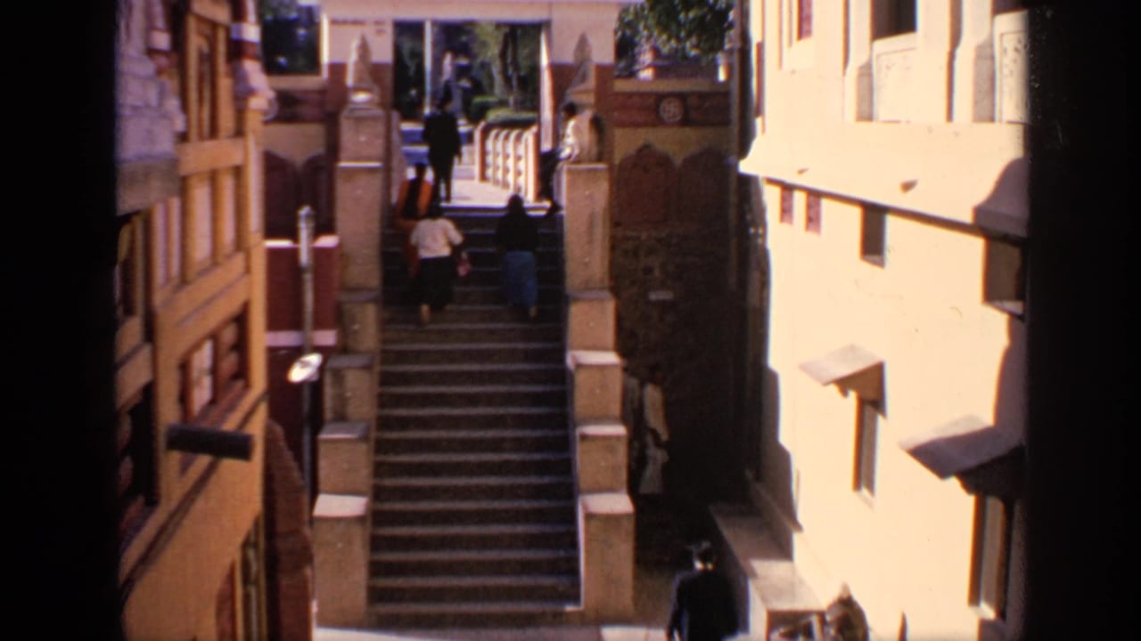 Visitors climb a wide stone staircase between sunlit ornate buildings.