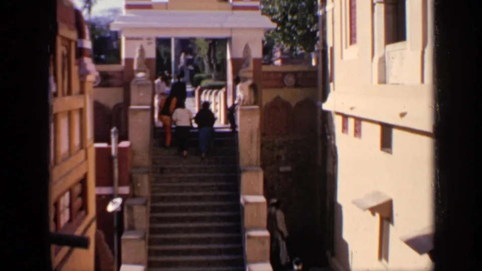 Distant 1970 India travel frame of visitors climbing steps toward a decorated gateway and building facade.
