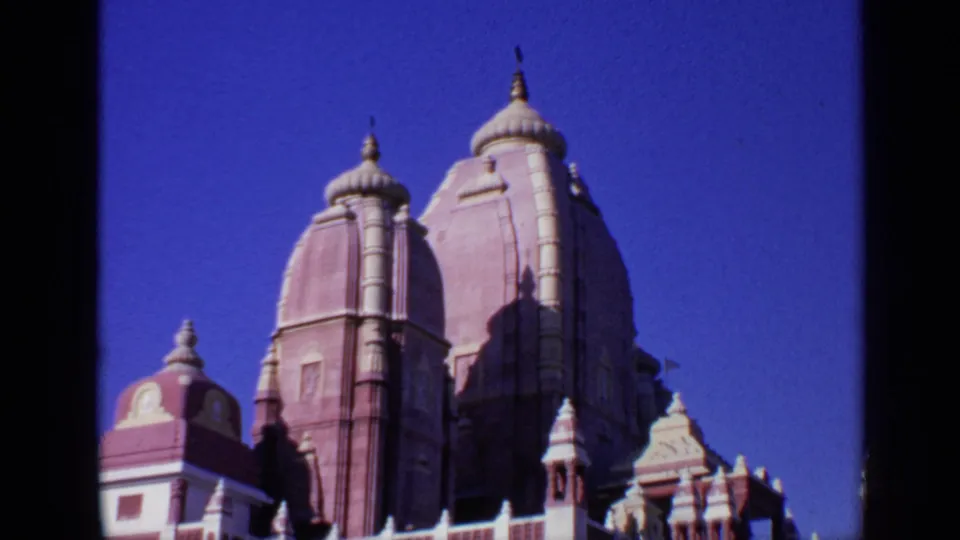 1970 India 8mm frame with temple spires rising above a wall and women seated in the garden below.