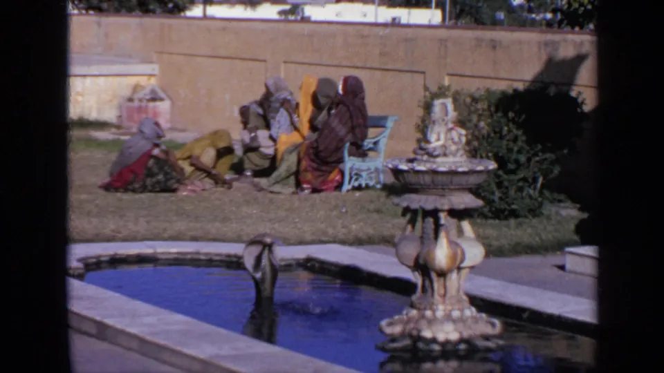 1970 India 8mm frame showing women in colorful clothing seated beside a garden pool and ornamental fountain.
