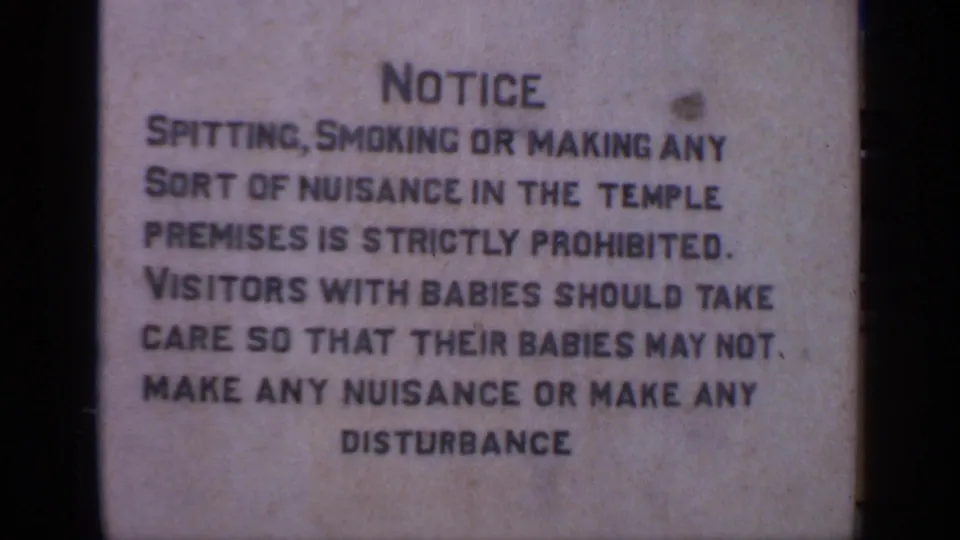 The 8mm frame shows a temple notice board listing conduct rules for visitors, including warnings about spitting, smoking, and disturbance.