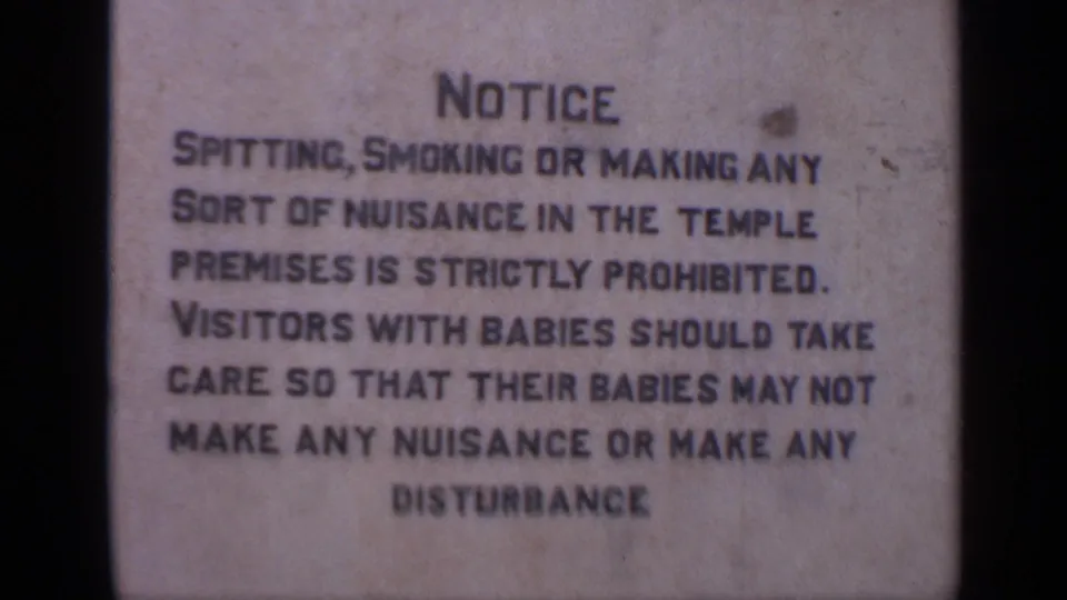 Close 8mm view of a temple regulations sign in India, with bold text about prohibited nuisance and visitor conduct.