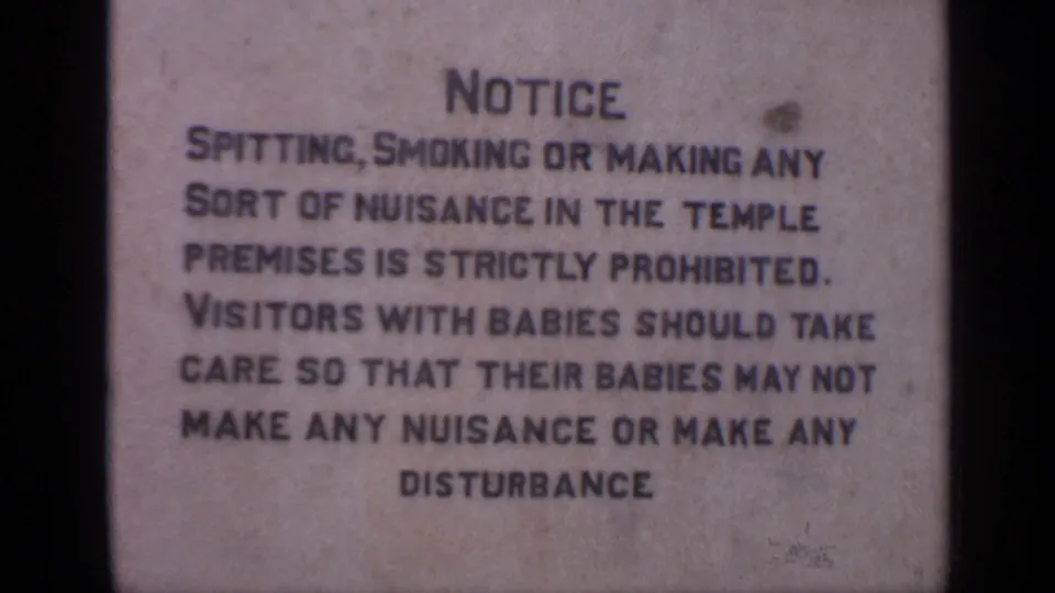 India 1970 home-movie frame with a close view of temple notice text warning visitors against nuisance or disturbance.