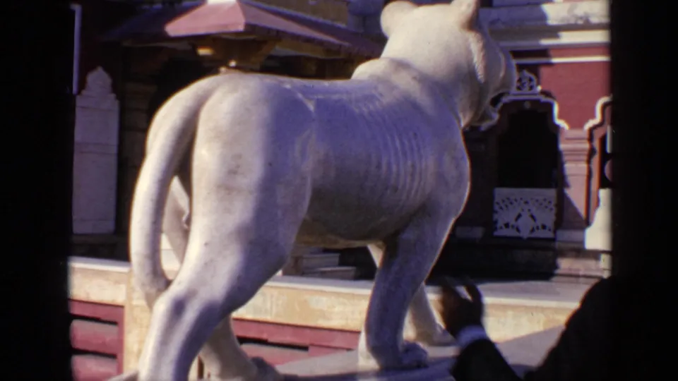 1970 India 8mm frame showing a white stone lion or mythical animal statue on a platform beside temple architecture.