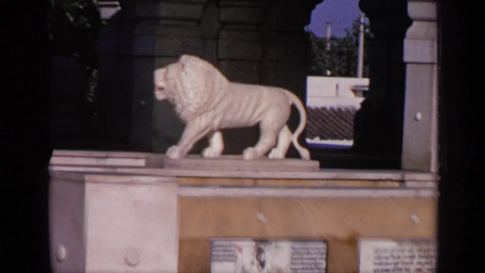 A tighter 8mm view shows the white lion statue on the temple pedestal, with plaques along the wall below.