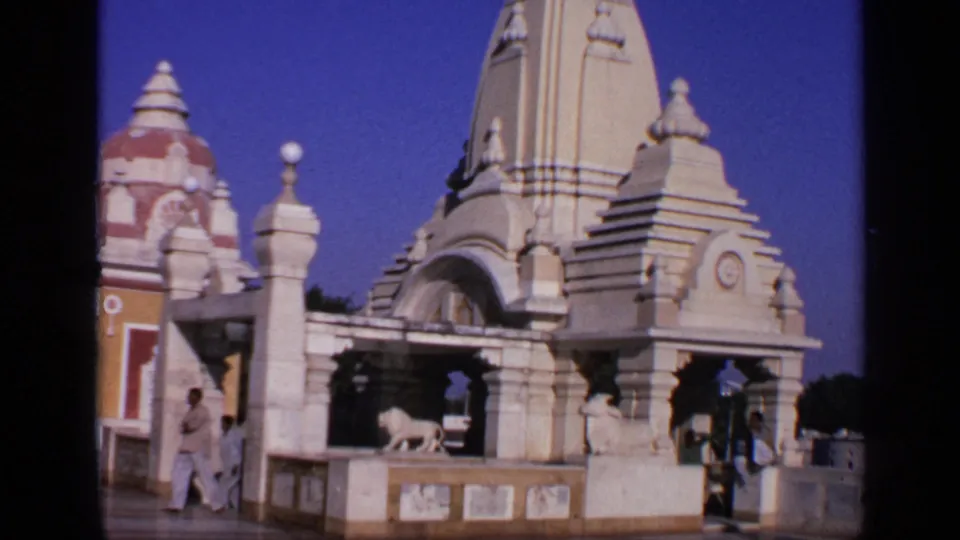 A wider 1970 India frame reveals the temple's domes and spires, the white lion statue, and visitors walking near the structure.