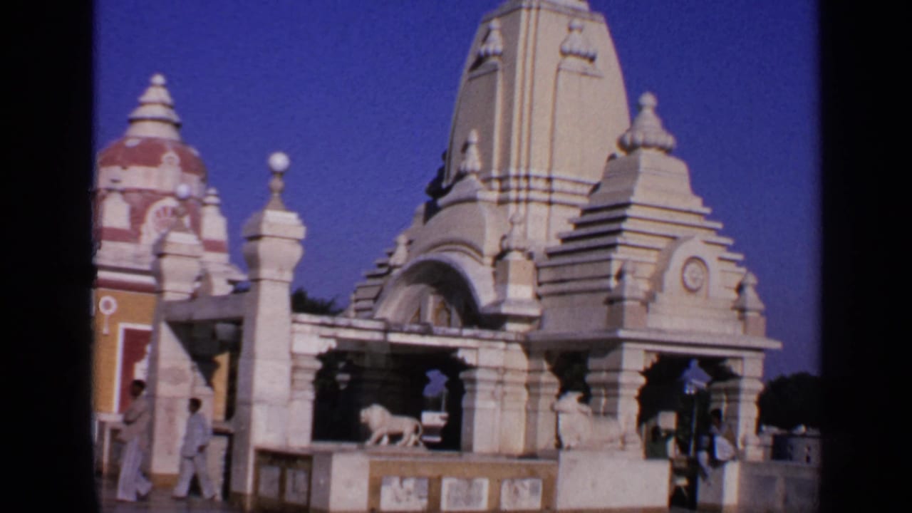 Temple complex with domed spires, lion statues, and visitors under a blue sky.