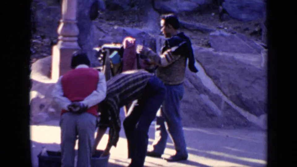 1970 India 8mm frame showing several men beside a bucket or basin near stonework, suggesting washing or preparation before entering.
