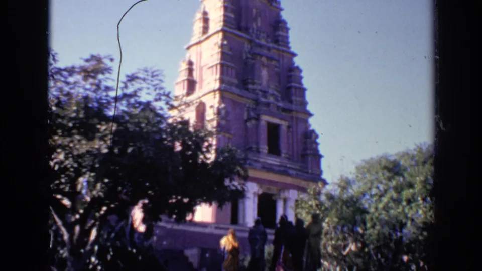 1970 India 8mm frame showing visitors near a temple entrance, trees in front, and the carved tower rising above.