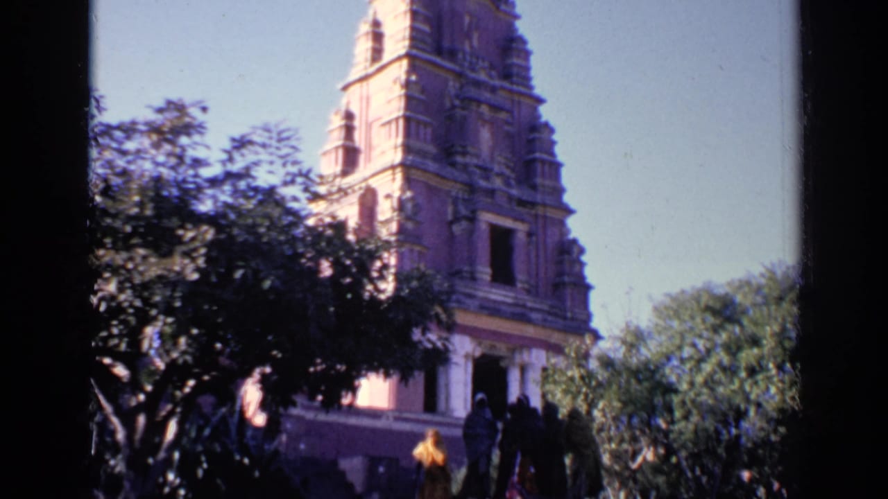 Ornate temple tower rising above trees in a sunlit courtyard.