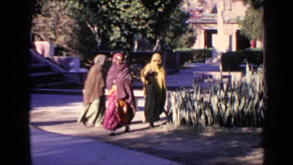 1970 India 8mm frame showing women in colorful traditional attire moving through a sunlit temple courtyard.