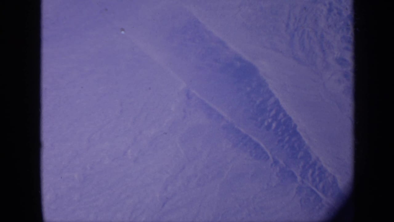 Aerial view of pale desert terrain beside dark aircraft-window framing.