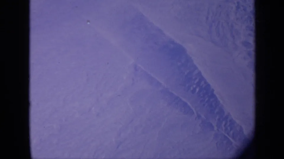 1970 India 8mm aerial frame showing pale desert terrain and faint ridges through a dark aircraft-window edge.