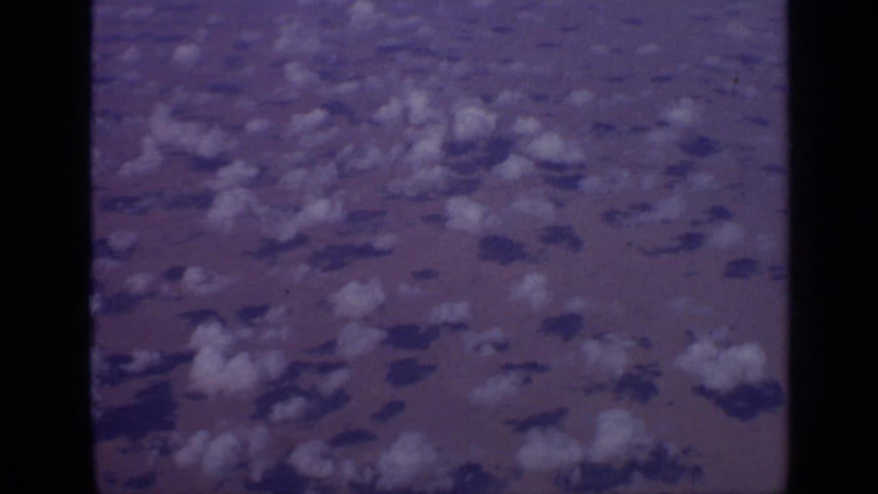 Scattered clouds and shadows over reddish desert terrain from above.