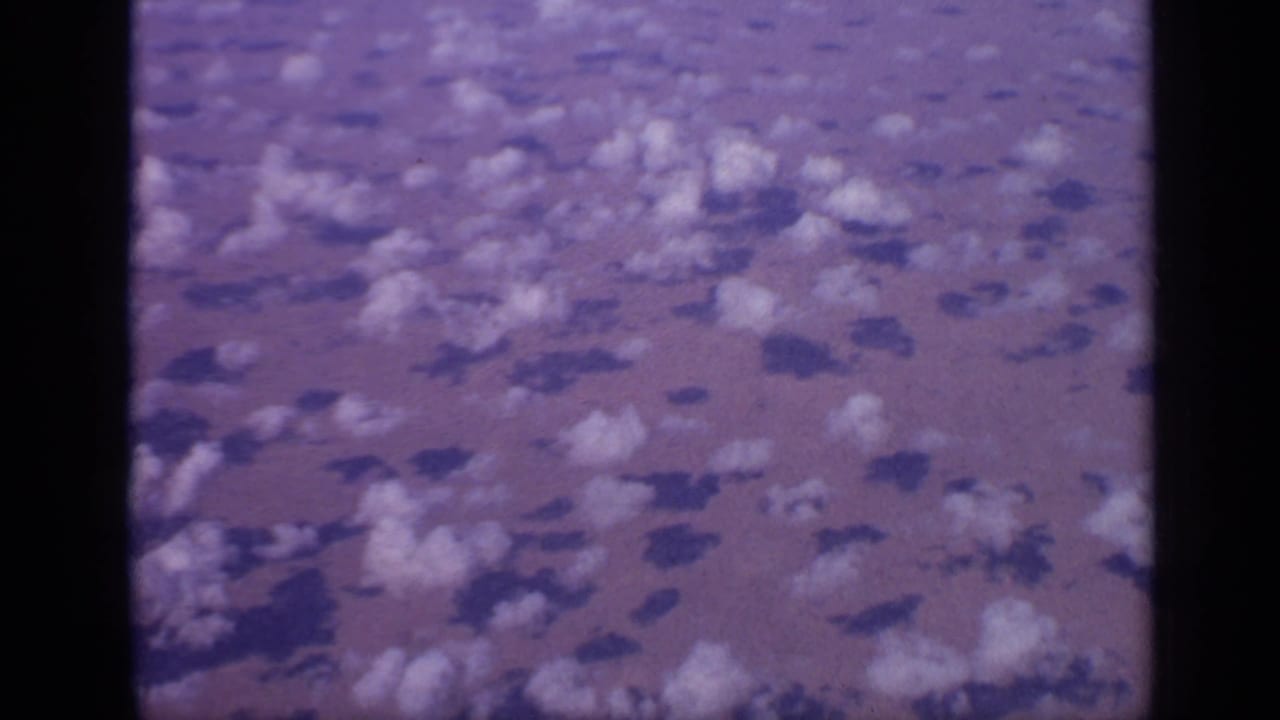 Clouds and cloud shadows over hazy land, seen from above with dark film borders.