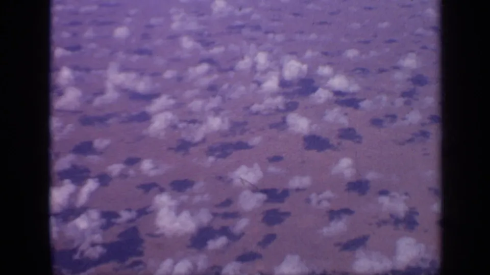 Aerial 8mm view over India showing broken white clouds and their shadows across the surface below, with strong purple film color shift.