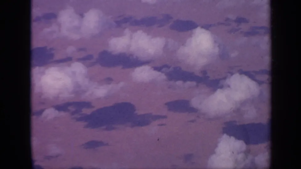 Aerial 8mm frame from India showing larger clouds in the foreground with darker shadows on the surface below and a soft purple cast.