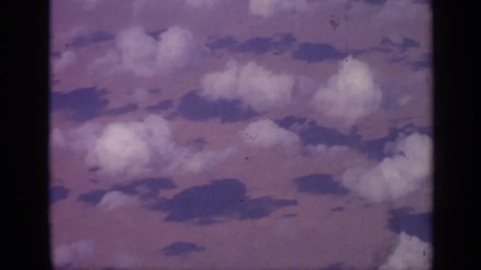 Passenger-window view of clouds in 1970 India travel footage, with dark aircraft window framing and vintage 8mm color shift.