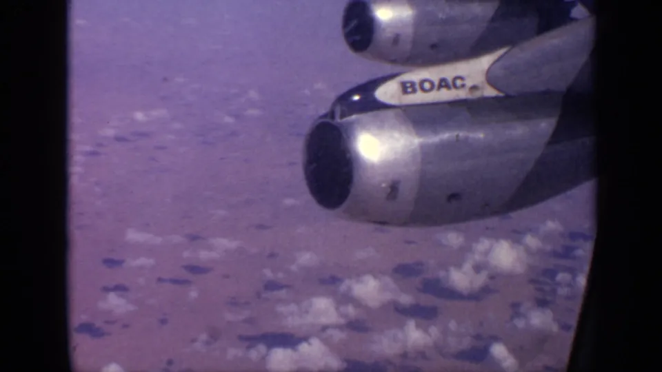 In-flight airplane window view with BOAC branding on the aircraft section, jet engines, and cloud cover below.