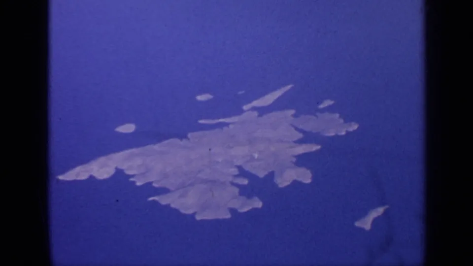 1970 8mm aerial view over India showing island shapes in blue water, framed by the dark edge of an aircraft window.