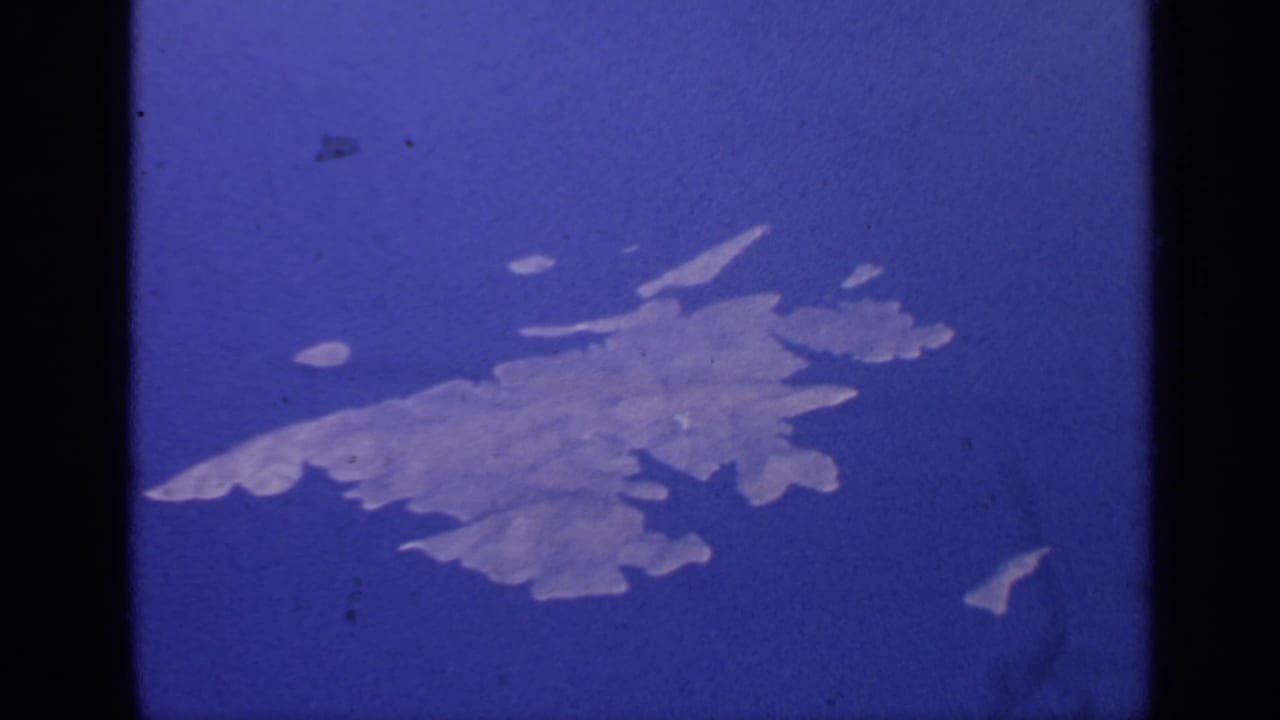 Similar aerial view of a pale island with small offshore shapes in blue water.