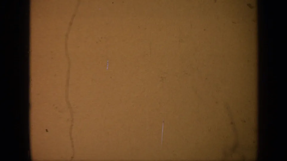 Amber-toned 8mm film surface with no clear subject, showing scratches, dust, and dark gate edges near the end of the roll.