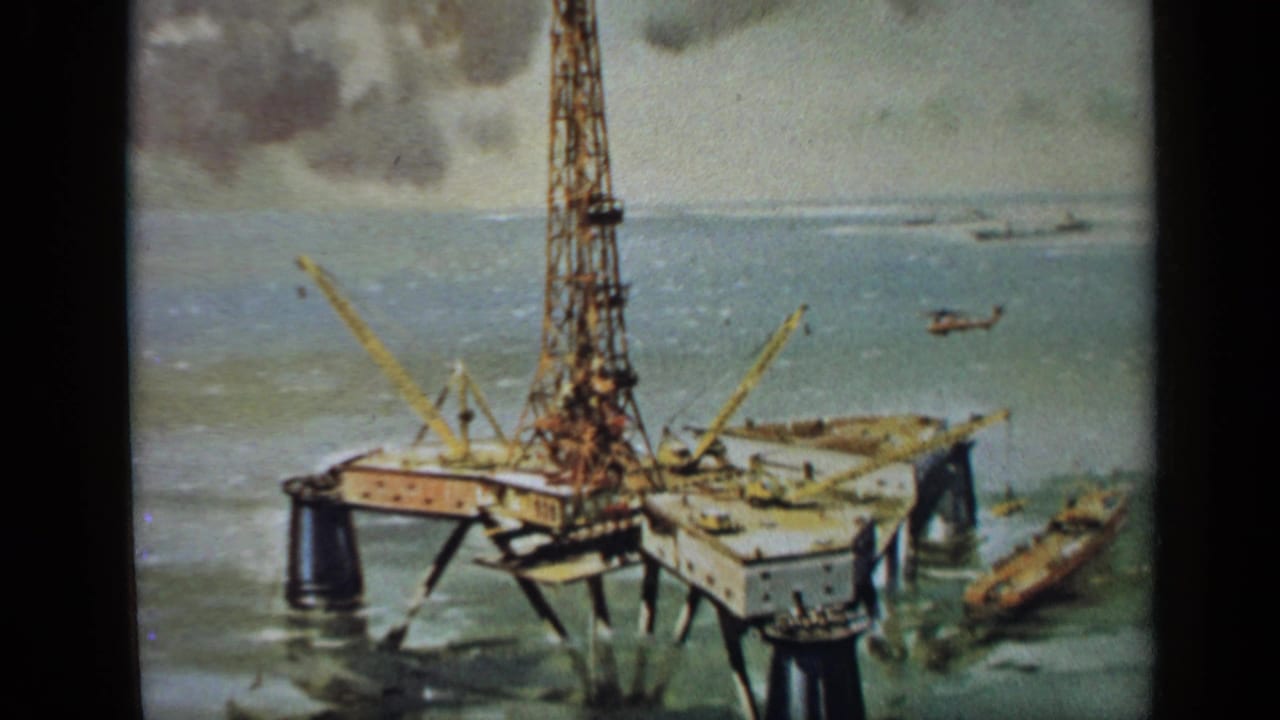 Painted offshore oil rig with cranes, boat and helicopter over open water.