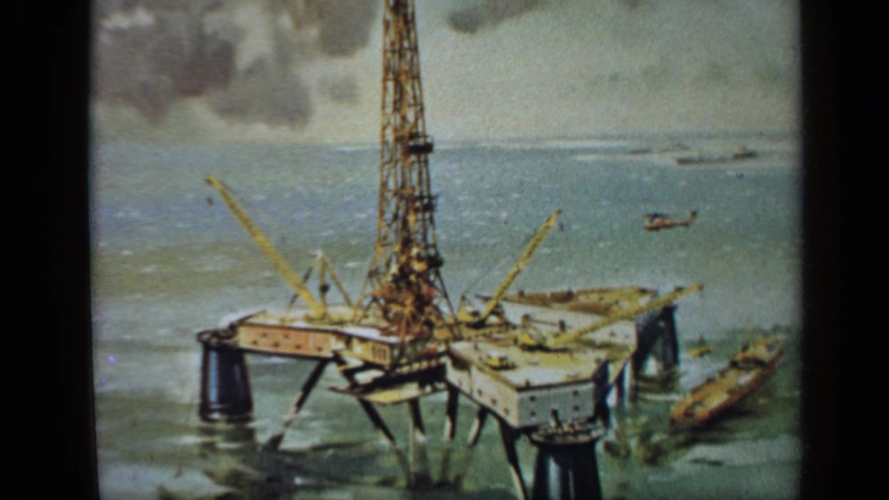 Offshore drilling platform with tall derrick, cranes, sea, and small helicopter.