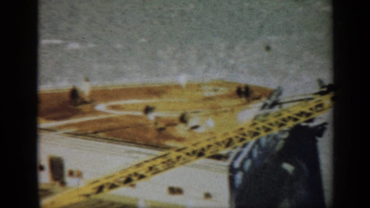 High-angle view of an offshore rig deck with a yellow crane structure and dark film-frame edges.