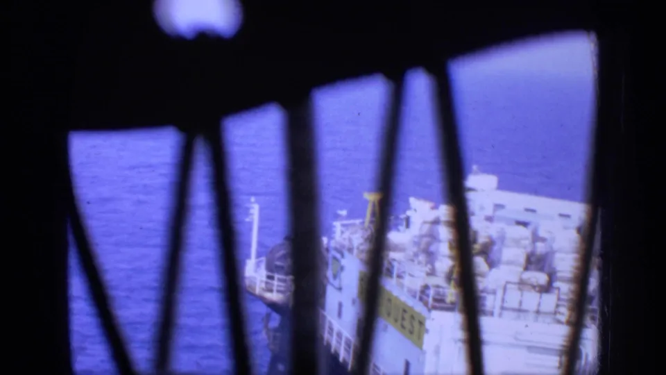 Obstructed 8mm view of the SEA QUEST vessel on open water, framed by dark vertical bars.