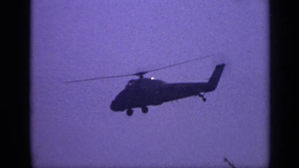 Soft 8mm view of a helicopter flying through a purple-blue sky near the end of the clip.
