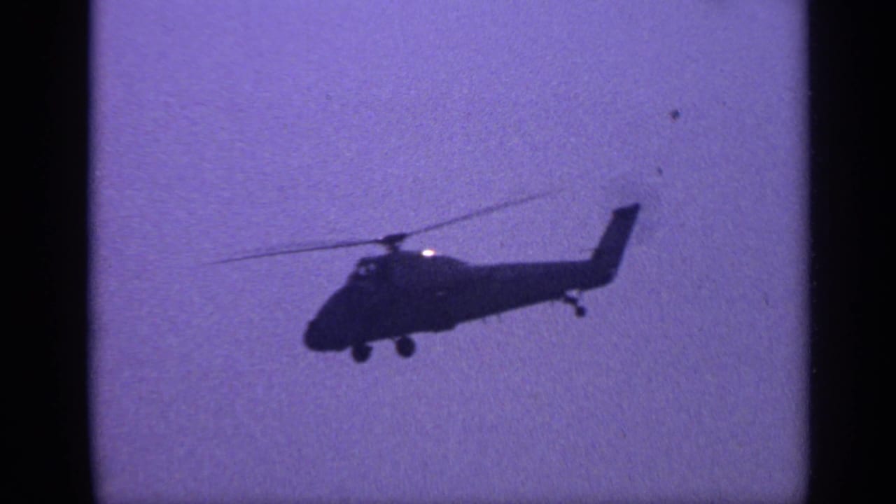 Dark helicopter silhouette flying across a hazy purple-blue sky.