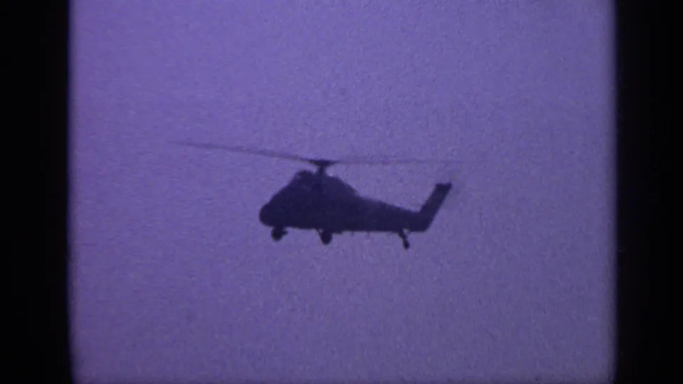1970 United Kingdom 8mm frame with a dark helicopter silhouette and spinning rotor visible against an open sky.