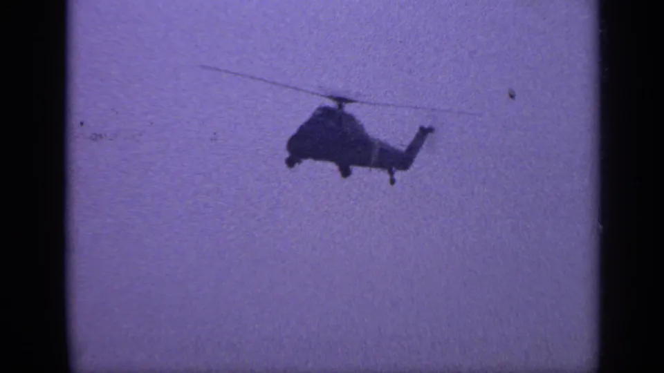 1970 United Kingdom 8mm frame showing the helicopter at a slight angle, reduced in size against the hazy sky.