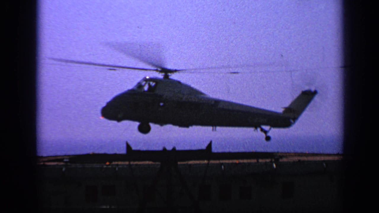Helicopter hovering just above the deck with rotor motion visible.