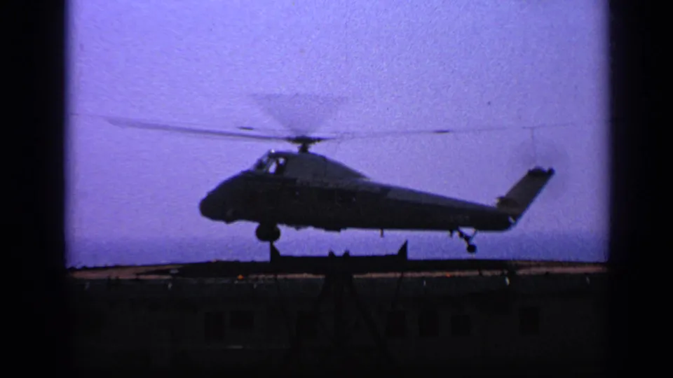 1970 United Kingdom 8mm frame showing the helicopter moments before touchdown on a ship or deck-like surface.
