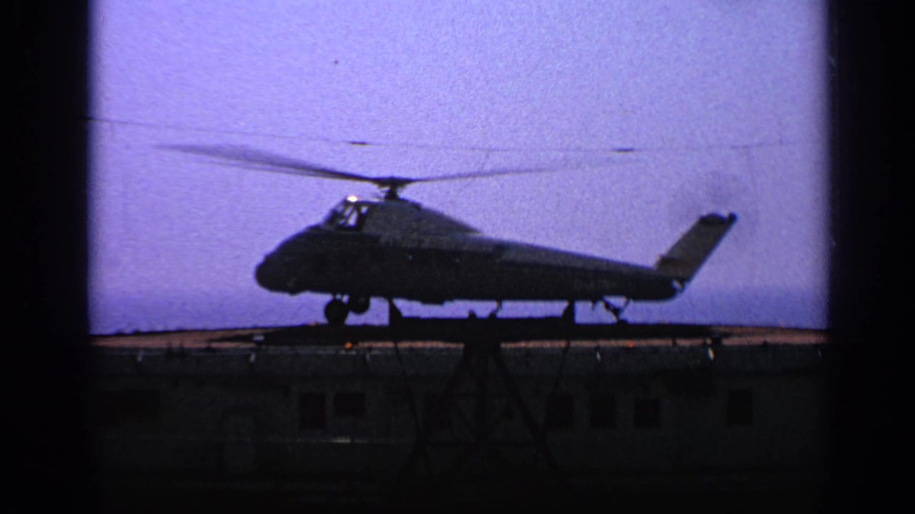 Silhouetted helicopter on a small platform against a purple sky.