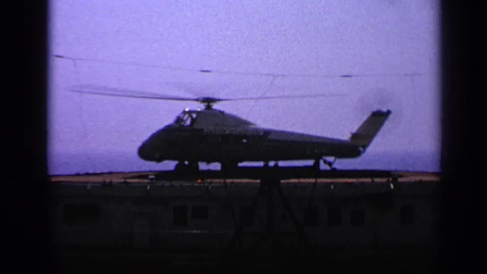 A silhouetted military helicopter sits or descends over a small platform in grainy 1970 United Kingdom 8mm footage.