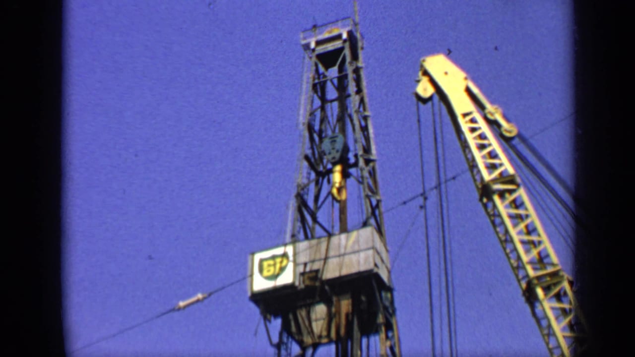BP-marked derrick and yellow crane boom against a blue sky.