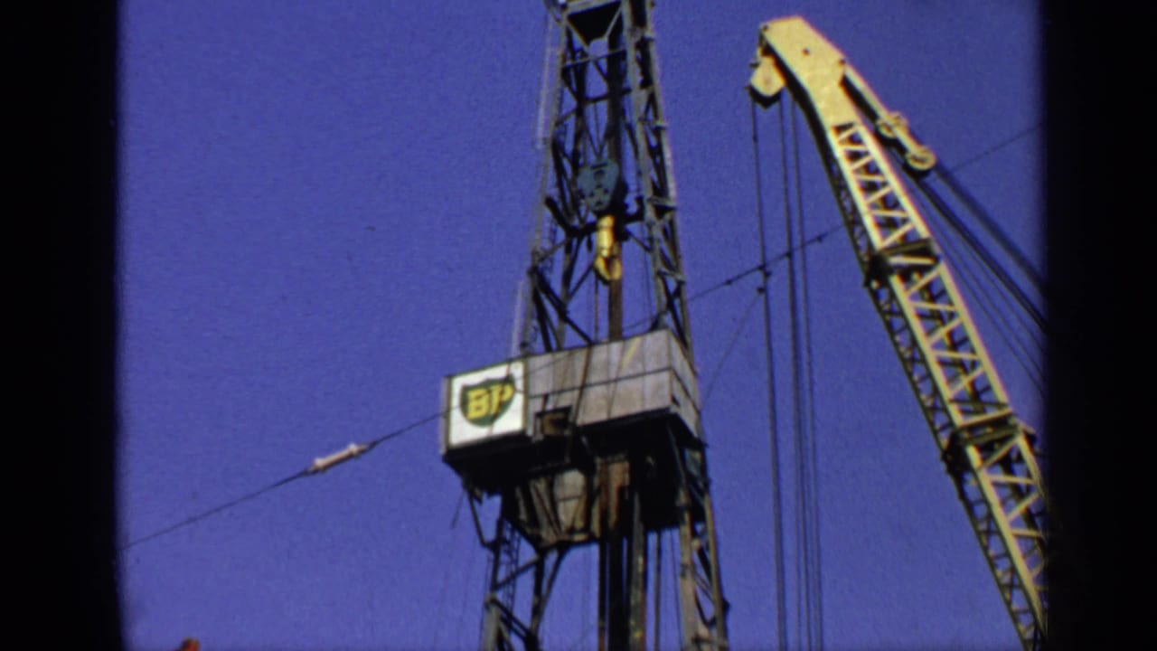 Oil derrick top and yellow crane framed by dark film borders.