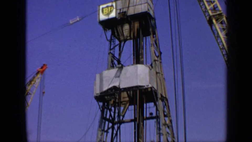 1970 United Kingdom Super 8 view of a BP-marked derrick, steel framework, cables, and a smaller crane at the edge of frame.