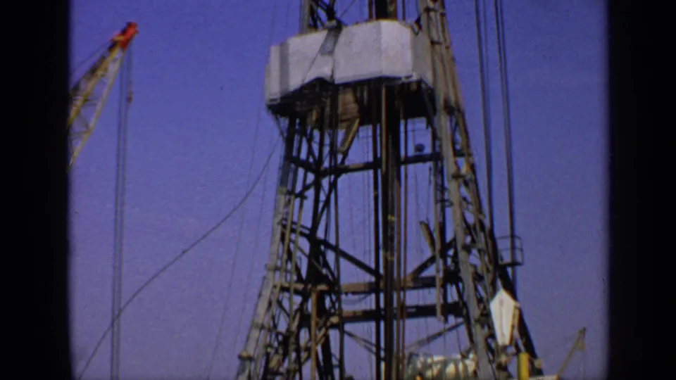 1970 United Kingdom Super 8 frame showing the derrick framework, suspended cables, and distant crane equipment, with BP branding less clear.