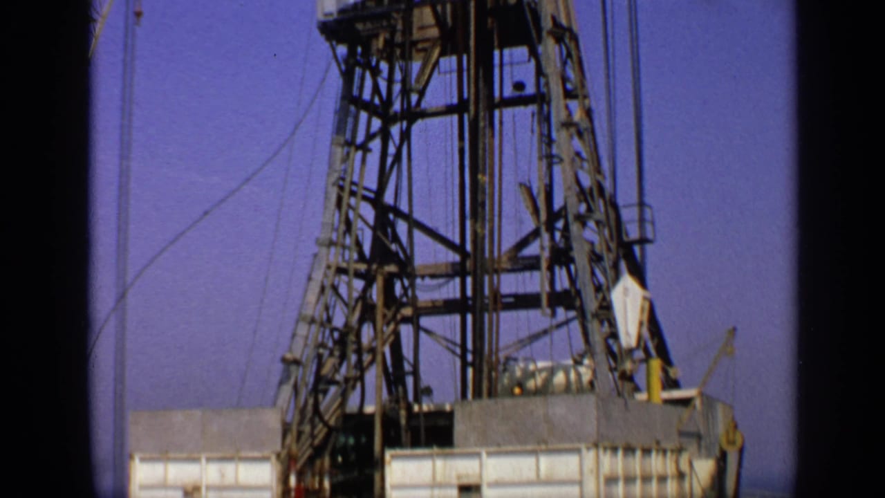 Tall offshore drilling rig derrick and deck structure under a blue sky.