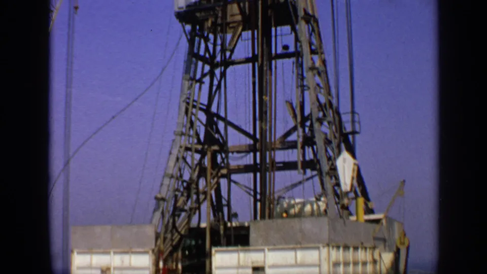 1970 United Kingdom 8mm frame showing the upper structure of an offshore drilling rig with derrick tower, cables and deck platform.