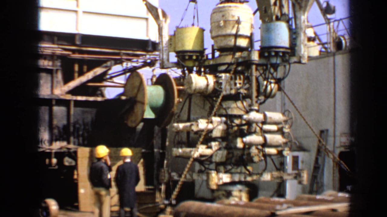 Two hard-hatted workers stand beside heavy machinery on an offshore platform.