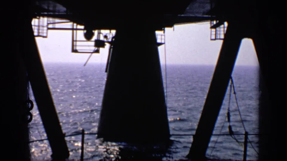 A 1970 8mm maritime view from the United Kingdom, with heavy silhouettes against bright water and a pale sky.