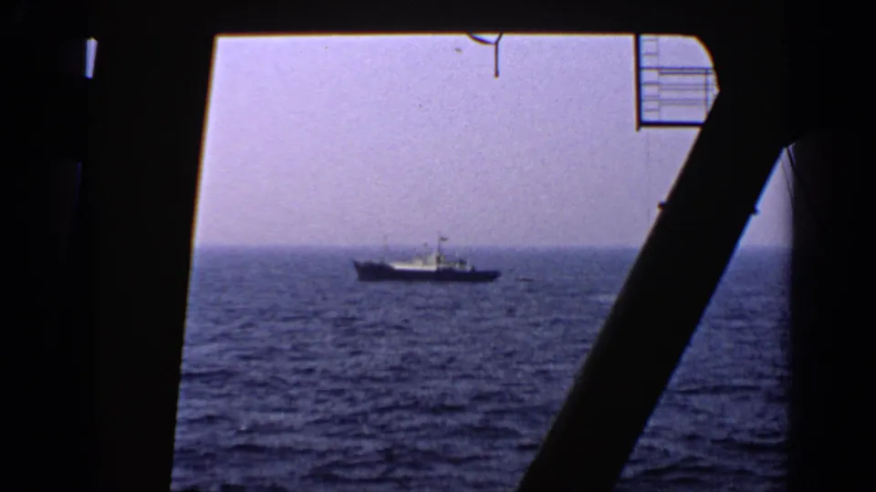 1970 United Kingdom 8mm frame with a distant vessel on open water, viewed through silhouetted ship or platform supports.
