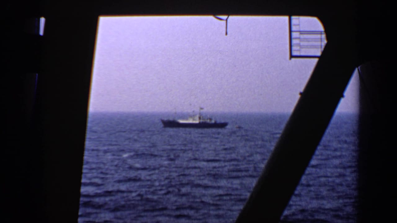 Distant vessel seen across the sea through a dark ship-window frame.