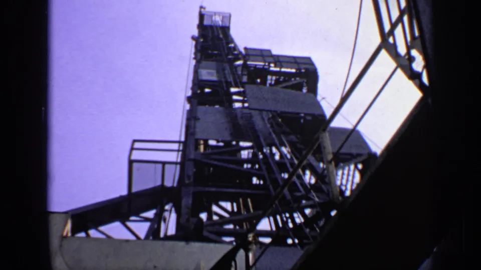 Low-angle 8mm view of a tall offshore rig or platform structure, with metal framework and railings silhouetted against the sky.