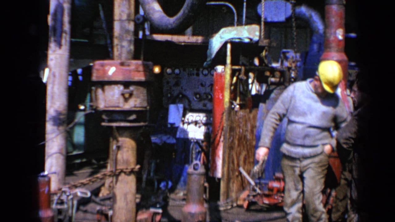 Worker in a yellow hard hat walking beside large industrial equipment and pipes.